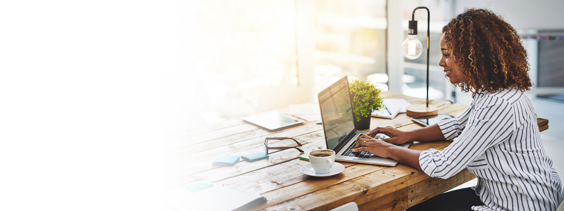 Woman using laptop with a coffee and sun shining