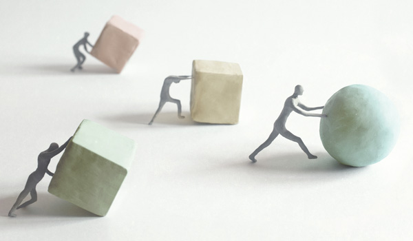 Three people pushing cubes, and one person ahead of them pushing a sphere